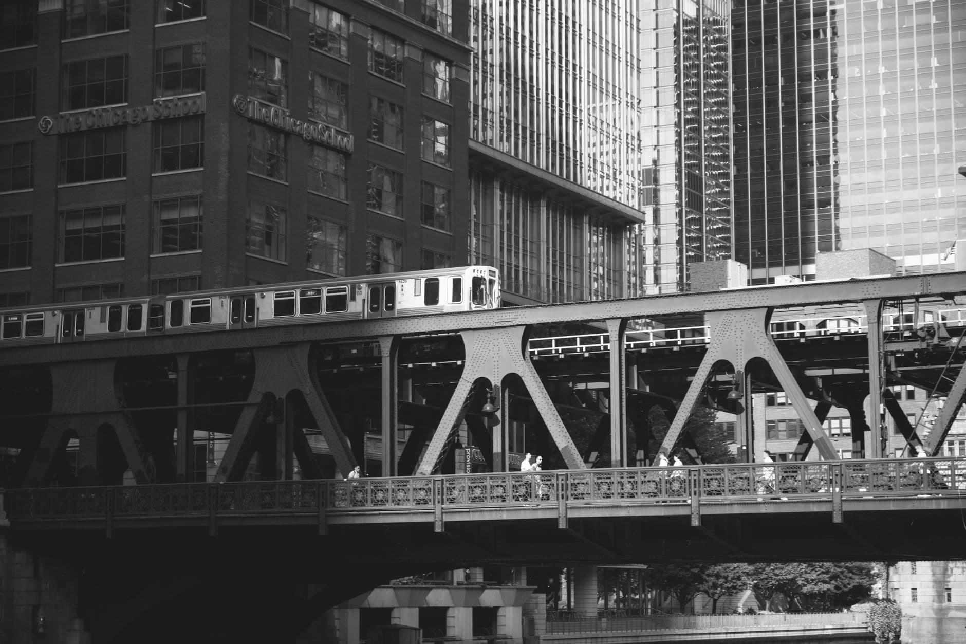 Black and white photo of a Chicago elevated train passing over a city bridge with skyscrapers in the background.